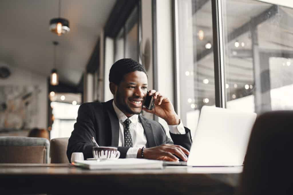 Business man on phone with laptop, notebook, and coffee in front of him.